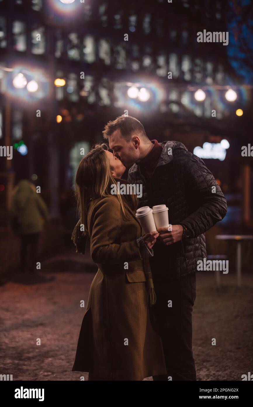 Coppia romantica con tazze usa e getta baciandosi di notte Foto Stock