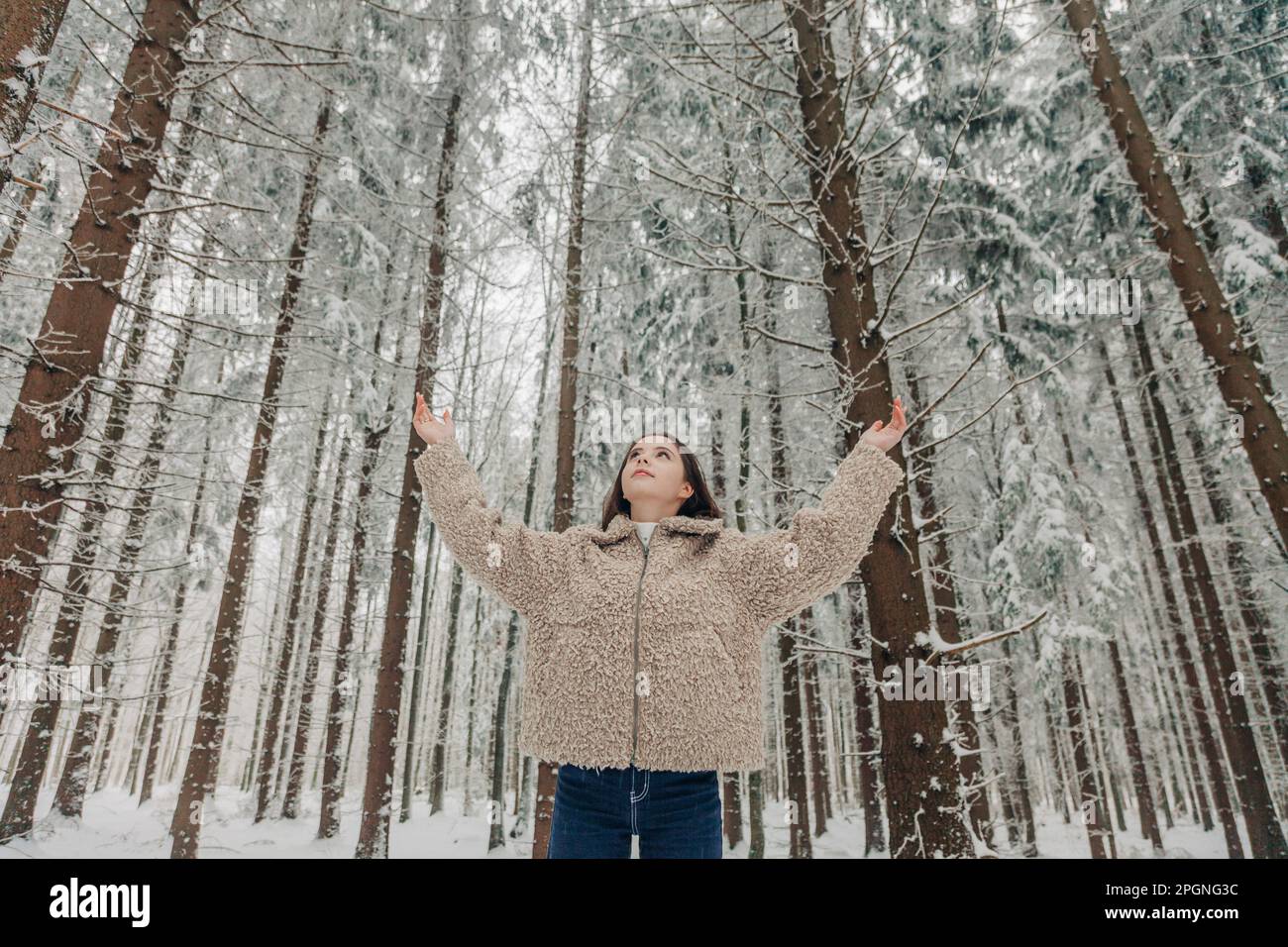 Ragazza adolescente con le braccia tese in piedi di fronte ad alberi alti Foto Stock