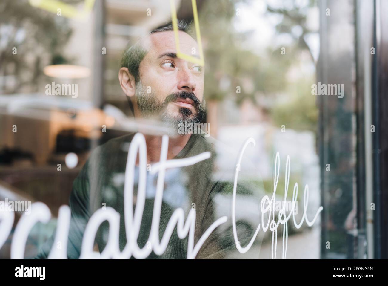 Uomo maturo e premuroso seduto in un caffè visto attraverso il vetro Foto Stock