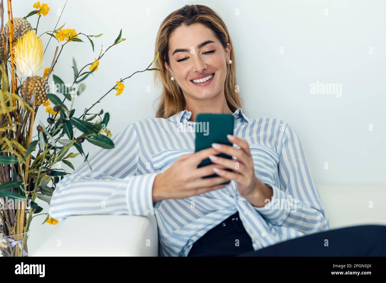 Messaggi di testo per una giovane donna felice grazie allo smartphone seduto sul divano Foto Stock