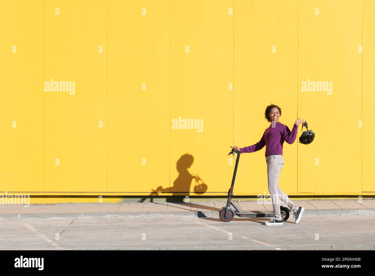 Donna con scooter elettrico sul sentiero davanti alla parete gialla Foto Stock