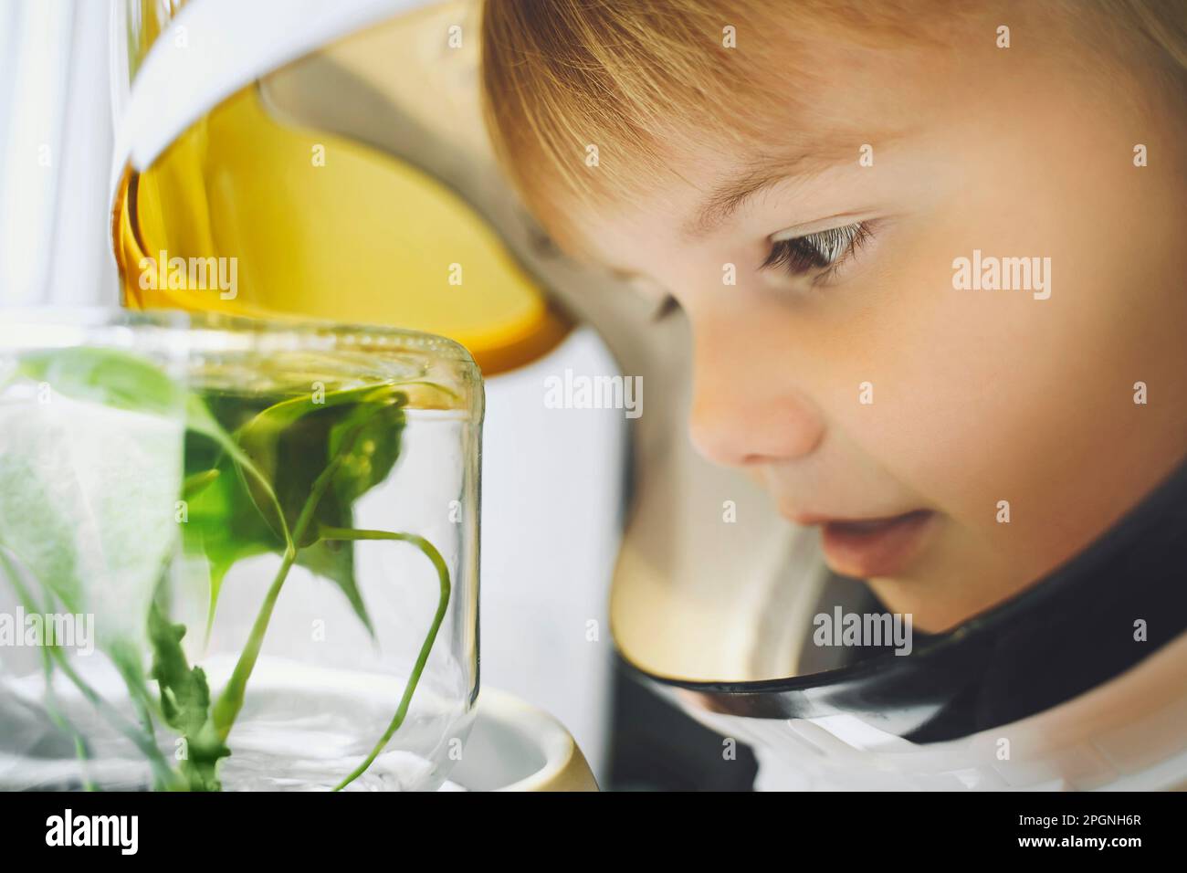 Ragazza che indossa il casco spaziale guardando la piccola pianta che cresce in vaso di vetro Foto Stock
