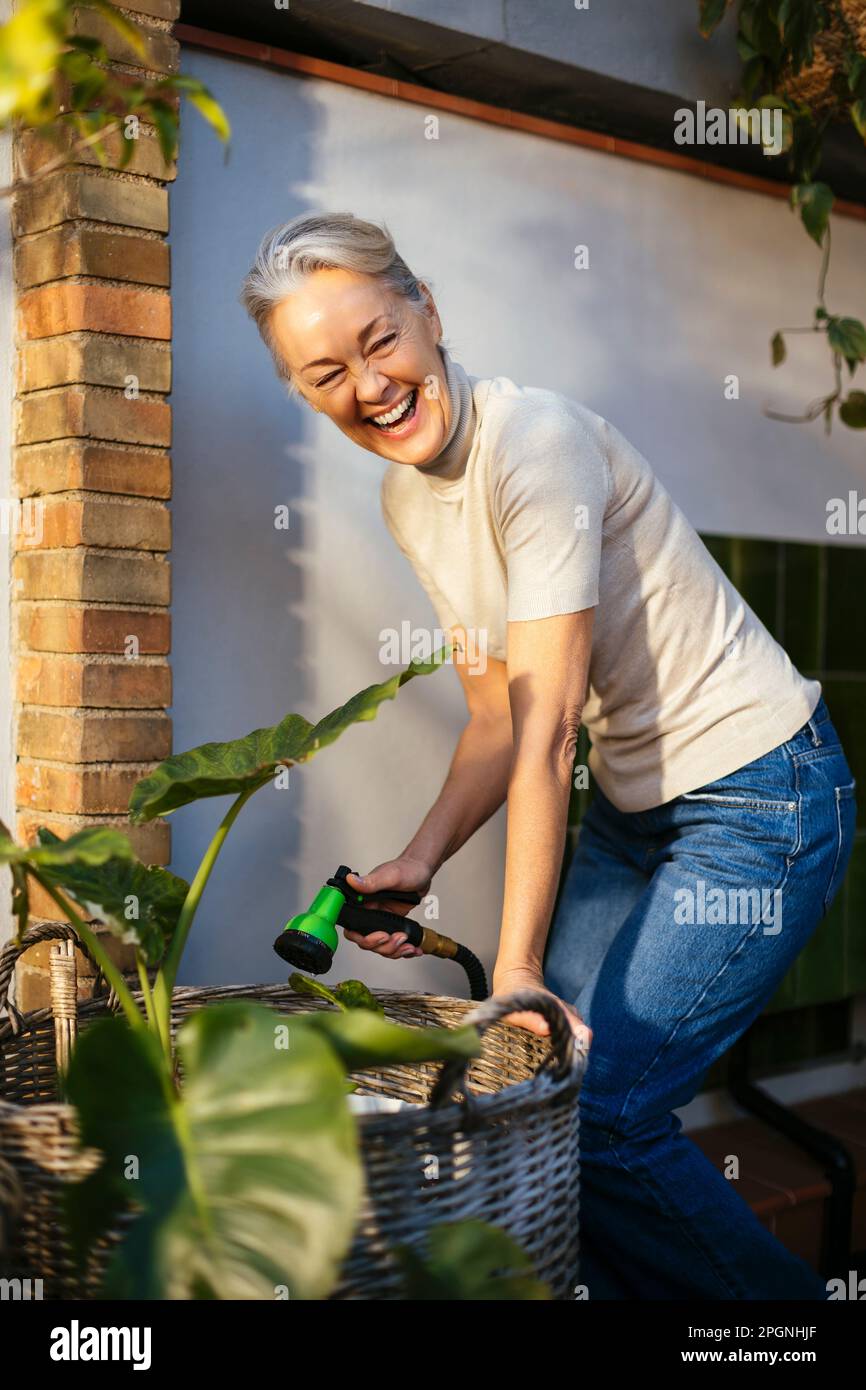 Donna matura felice che si prende cura delle piante Foto Stock