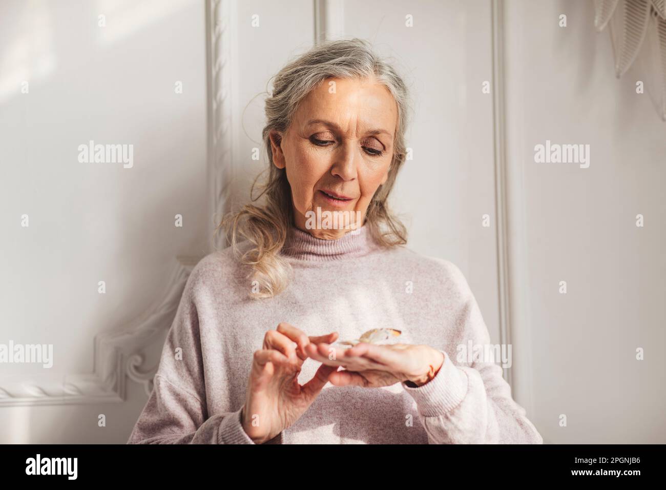 Donna anziana sorridente con farfalla a portata di mano a casa Foto Stock