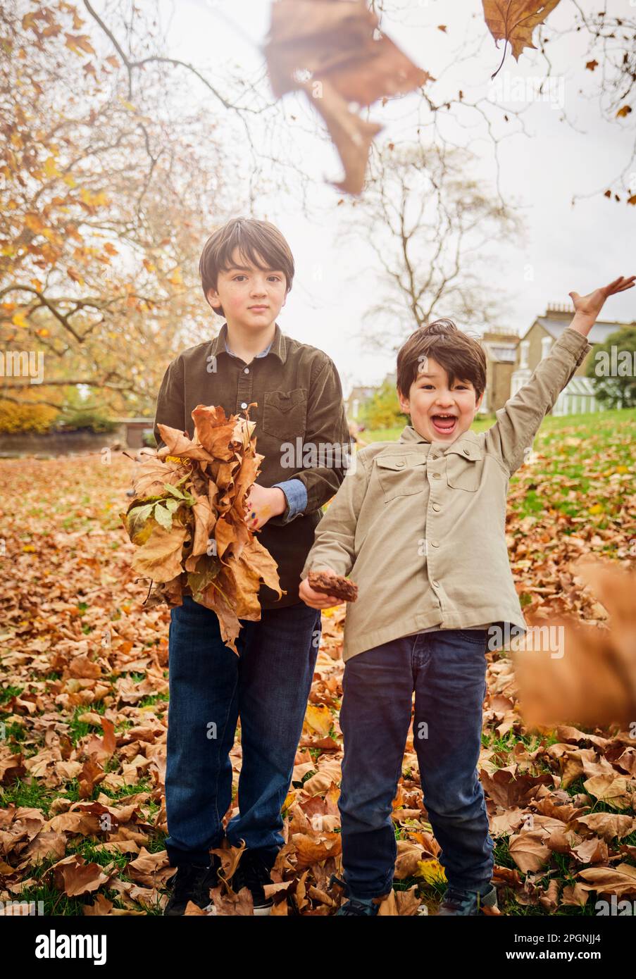 Ragazzi allegri che gettano via le foglie autunnali al parco Foto Stock