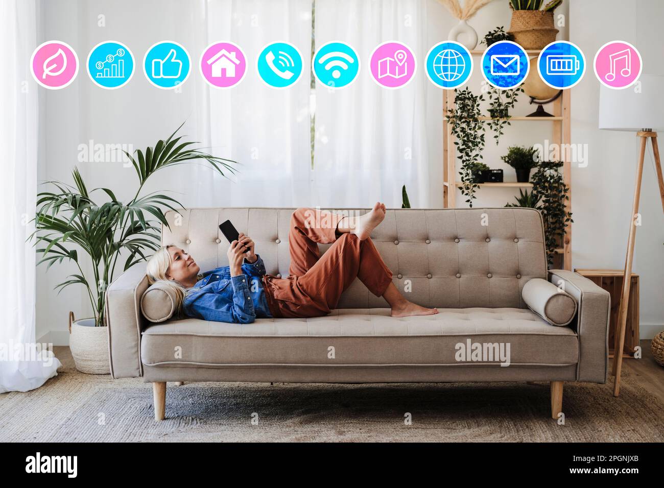 Donna sdraiata sul divano e che usa l'app per telefono cellulare a casa Foto Stock