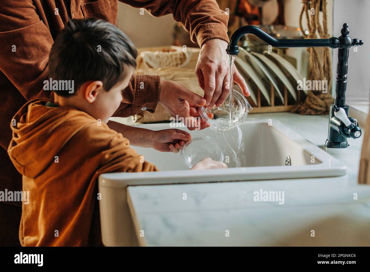 Figlio che aiuta padre nel lavaggio contenitore di plastica a casa Foto Stock