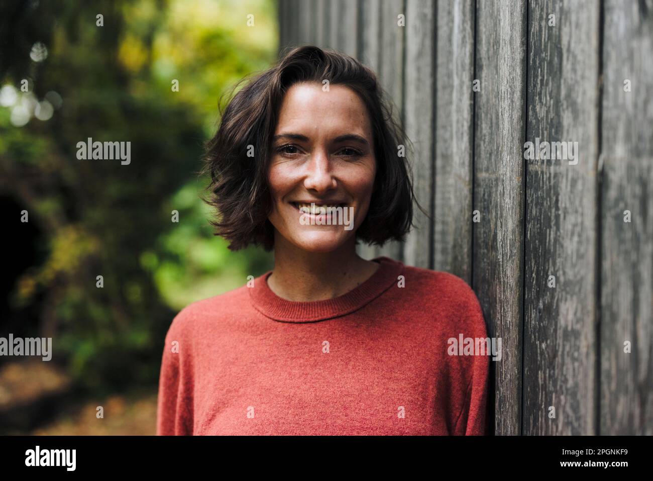 Donna sorridente con capelli scuri appoggiati al muro Foto Stock