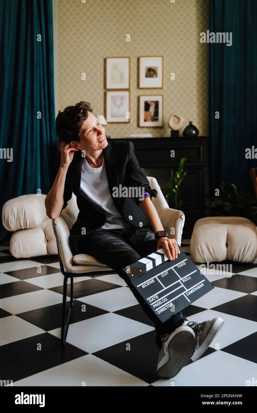 Sorridente regista seduto con clapboard su sedia al set cinematografico Foto Stock