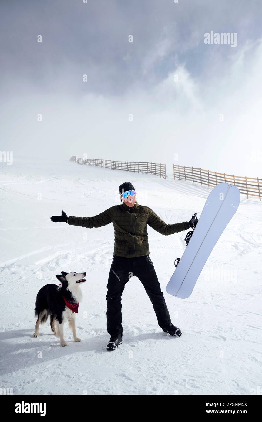 Uomo felice che tiene lo snowboard in piedi dal cane in vacanza Foto Stock