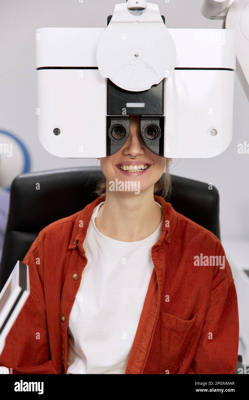 Paziente sorridente che fa il controllo dell'occhio in su attraverso il foropter alla clinica Foto Stock