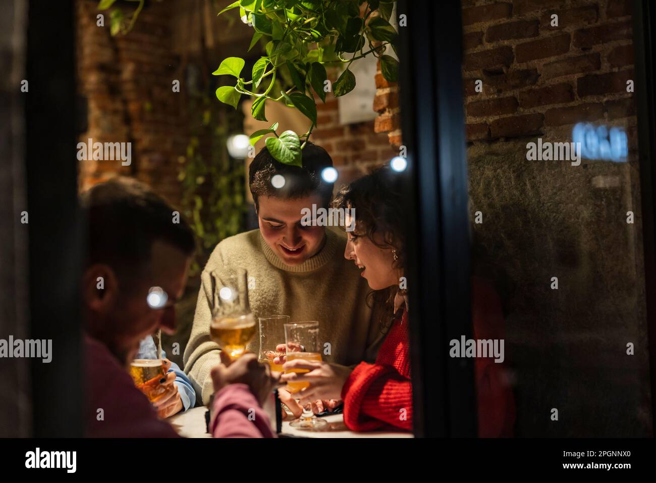 Amici con la birra che festeggiano nel ristorante fotografato attraverso la finestra Foto Stock