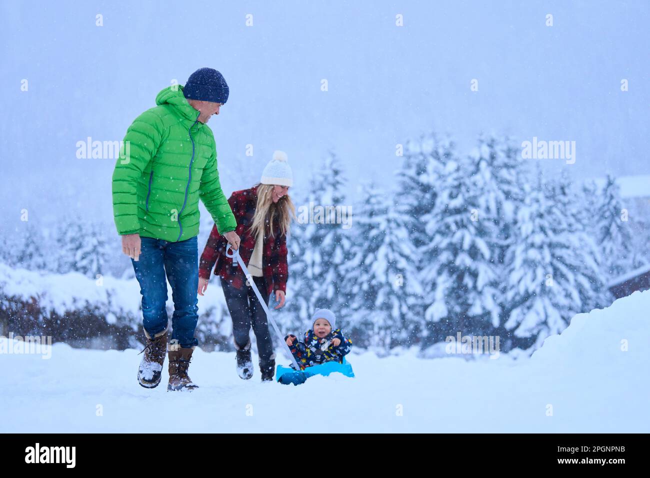 Madre e padre con figlio seduto sulla slitta nella neve Foto Stock