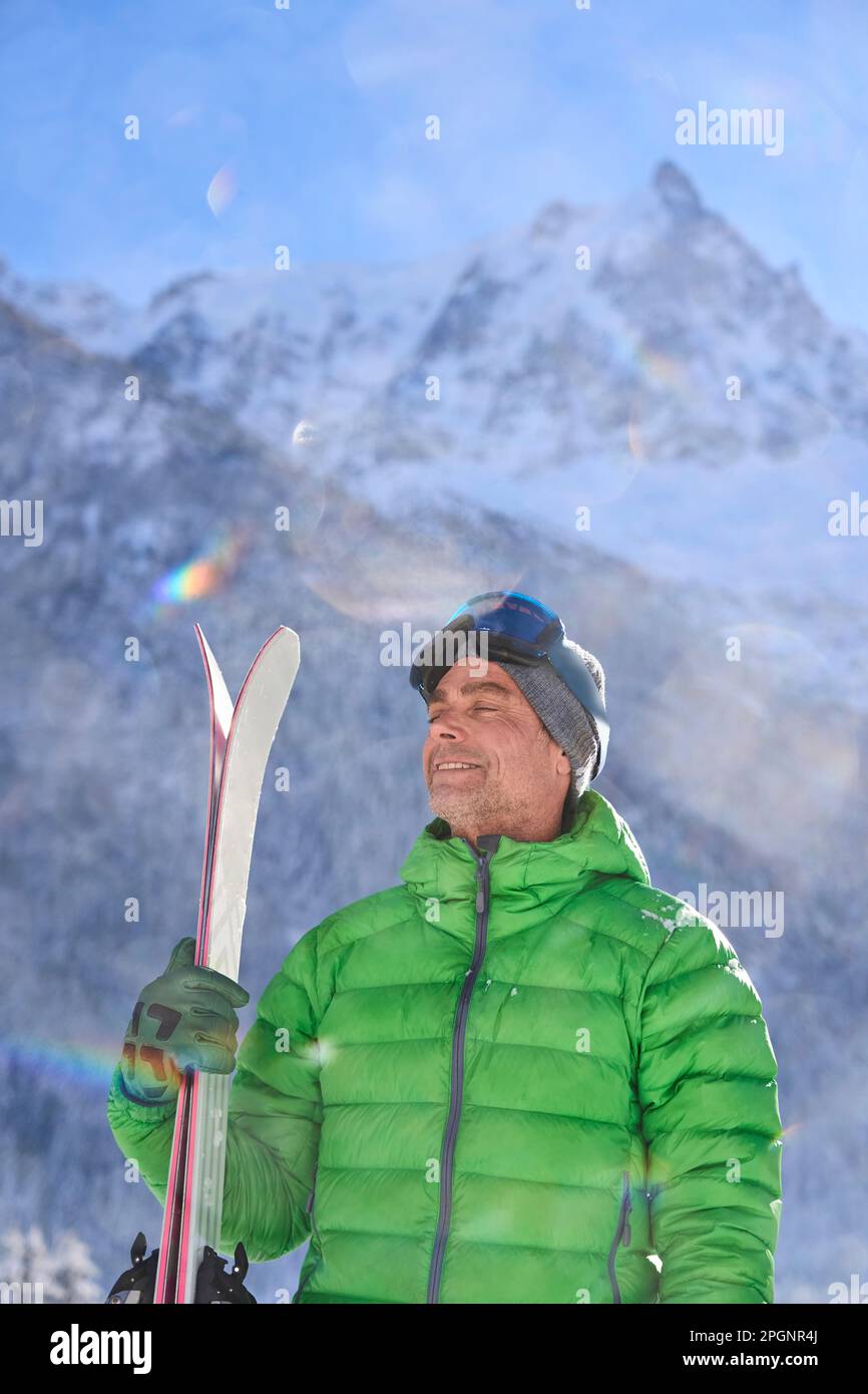 Uomo con gli occhi chiusi e gli sci in piedi davanti alle montagne Foto Stock