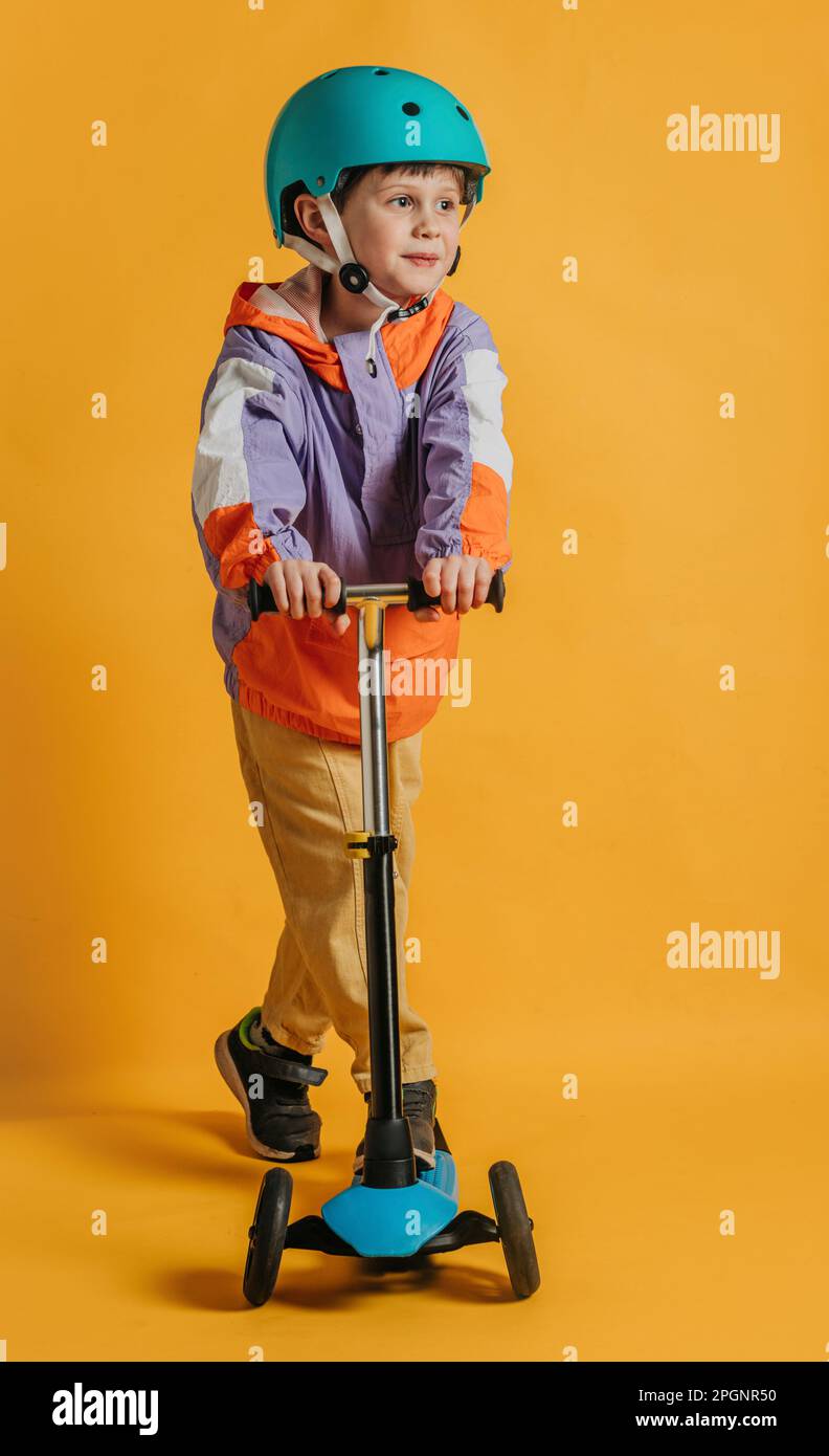 Ragazzo sorridente con uno scooter a spinta su sfondo giallo Foto Stock
