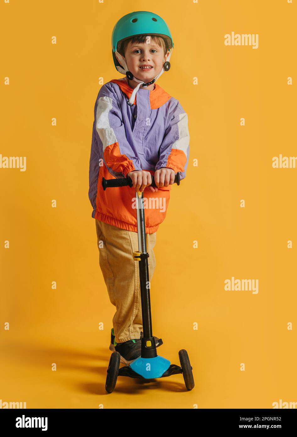 Ragazzo sorridente che indossa il casco in piedi con uno scooter a spinta contro lo sfondo giallo Foto Stock