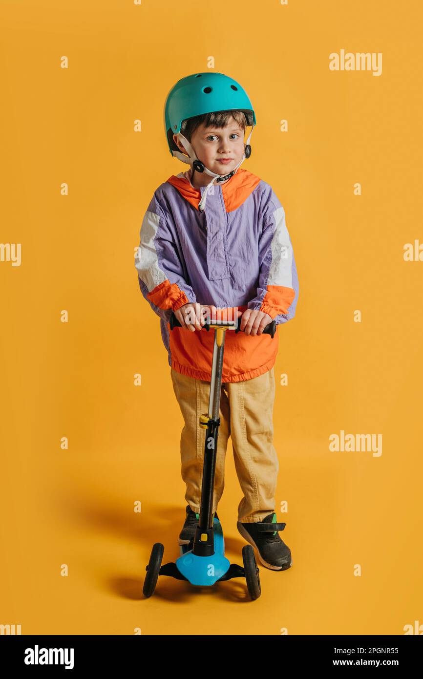 Ragazzo simpatico sorridente con scooter a spinta su sfondo giallo Foto Stock