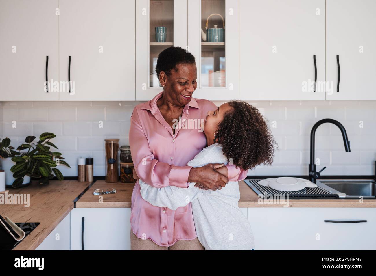 Nonna abbracciando la nonna in cucina a casa Foto Stock