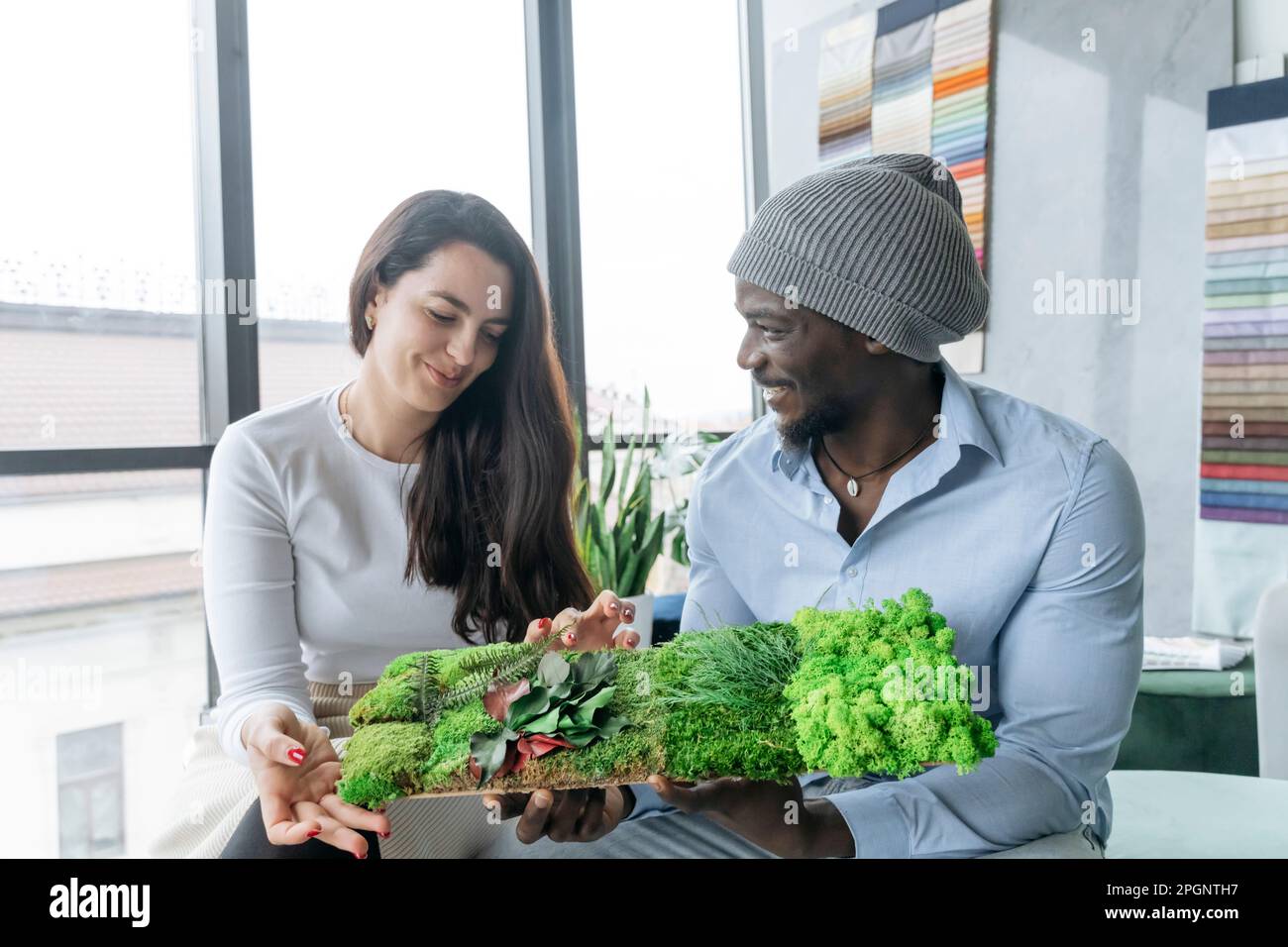 Sorridenti colleghi multirazziali che esaminano un campione di parete verde sul posto di lavoro Foto Stock