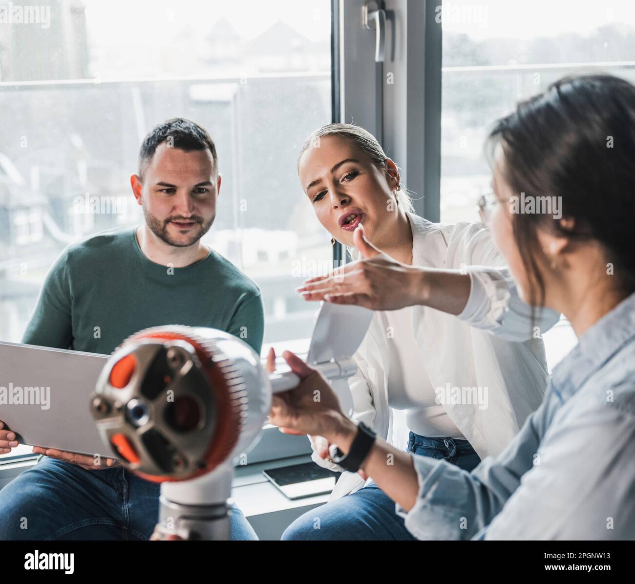 Donna d'affari che spiega le pale del rotore della turbina eolica ai colleghi in ufficio Foto Stock