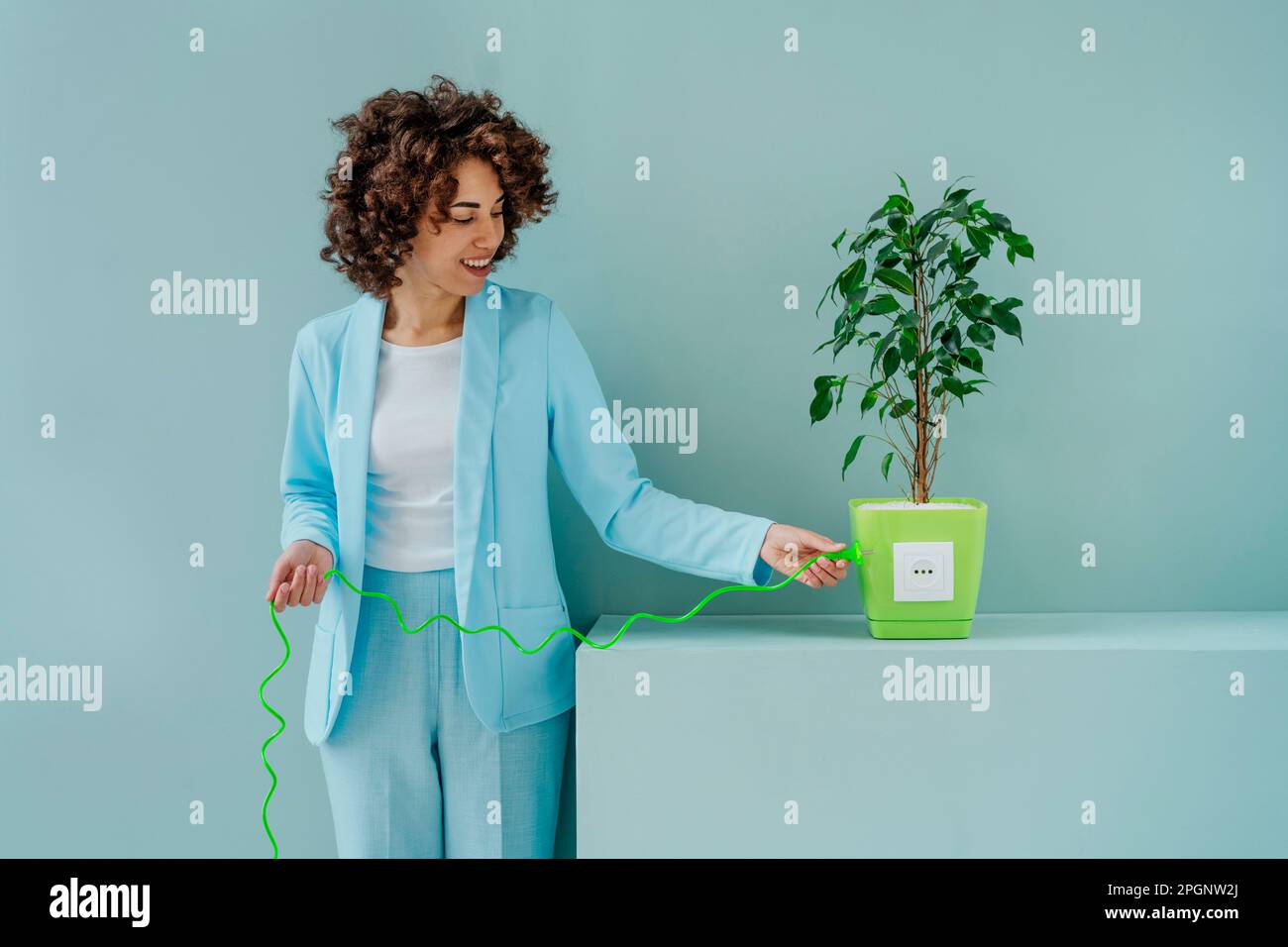 Donna sorridente che inserisce la presa collegata alla pianta in vaso Foto Stock