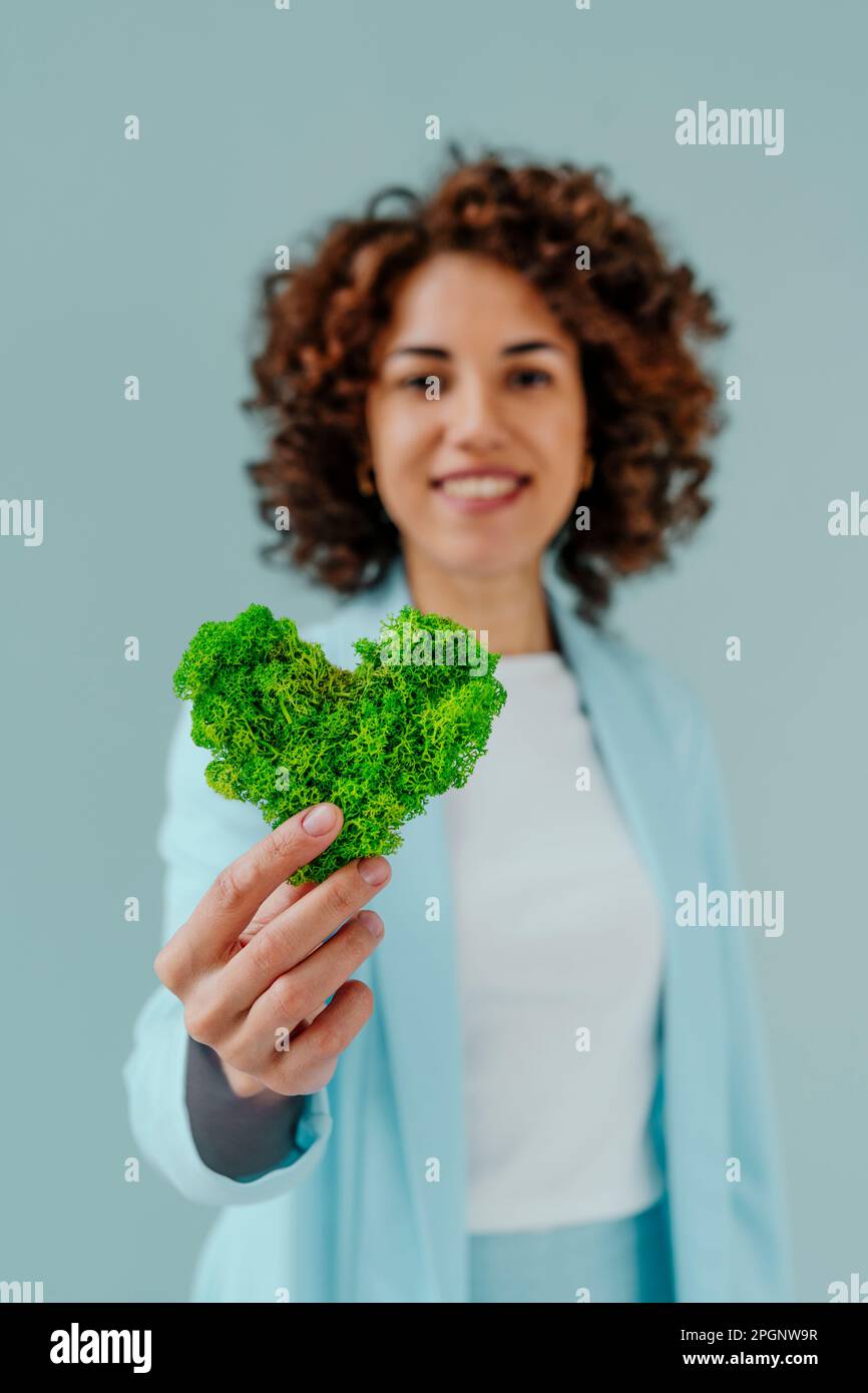 Donna che tiene verde cuore a forma di muschio su sfondo blu Foto Stock