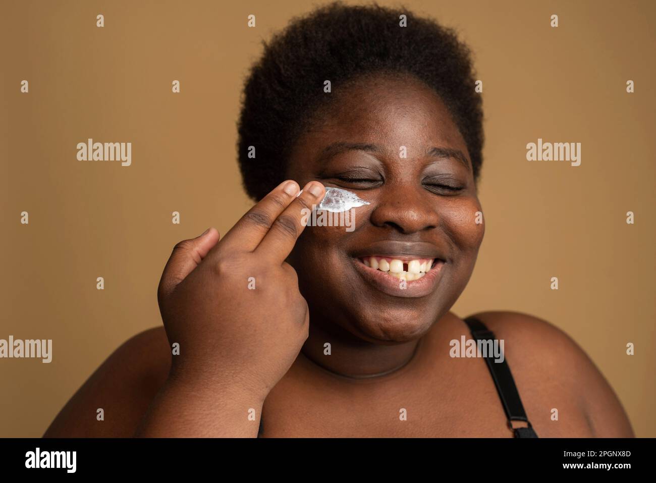 Più donna di misura che applica l'olio cosmetic sulla faccia contro lo sfondo beige Foto Stock