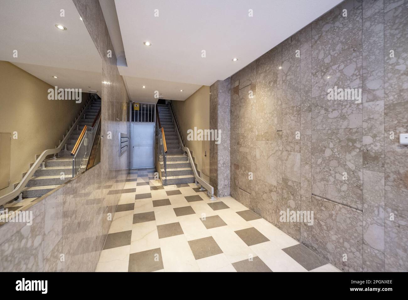 Portale di un edificio residenziale urbano con pareti in marmo, un grande specchio integrato nella parete e una scala con ascensore Foto Stock