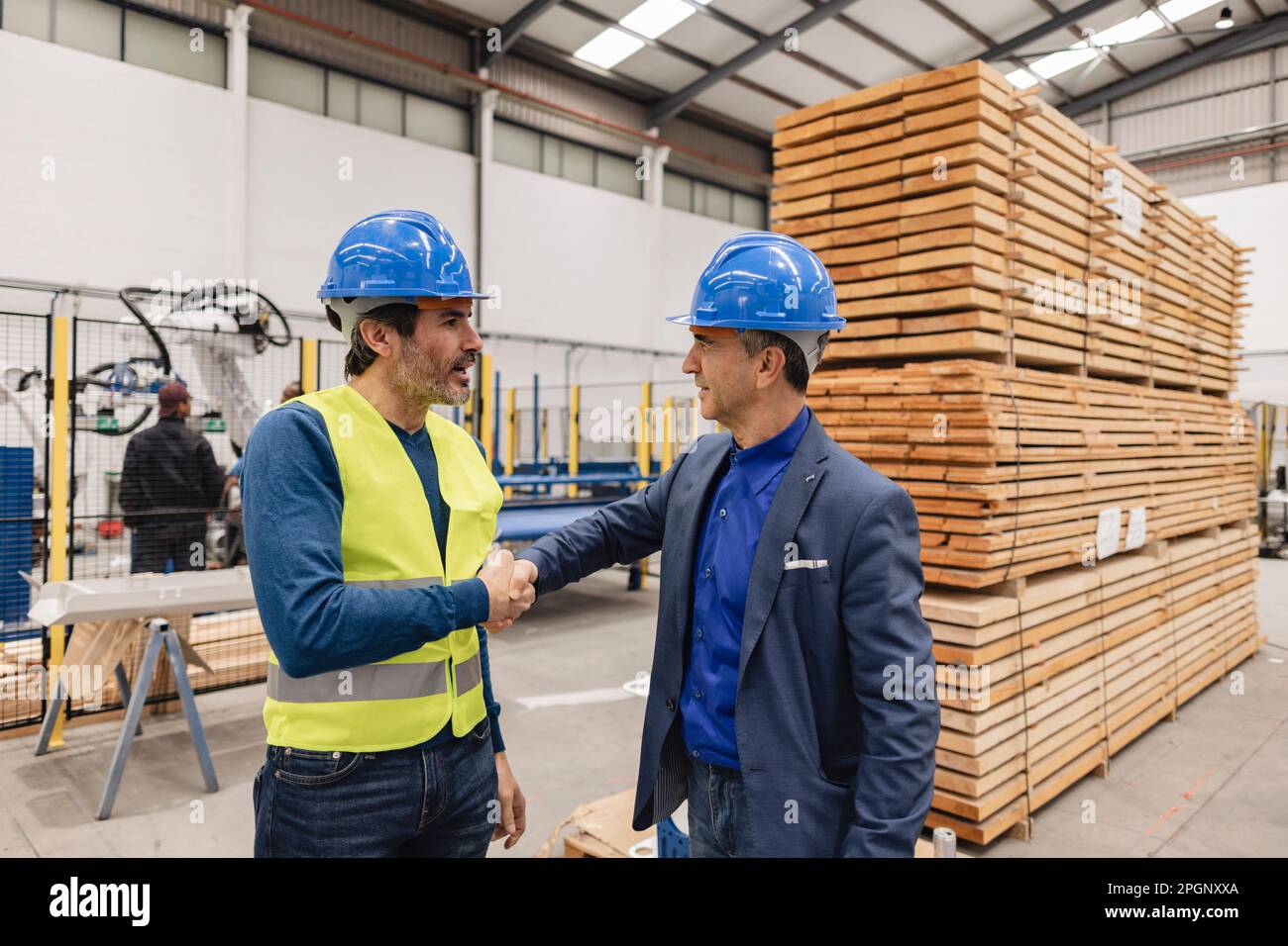Ingegneri maturi che indossano cappelli duri che fanno la stretta di mano in fabbrica Foto Stock