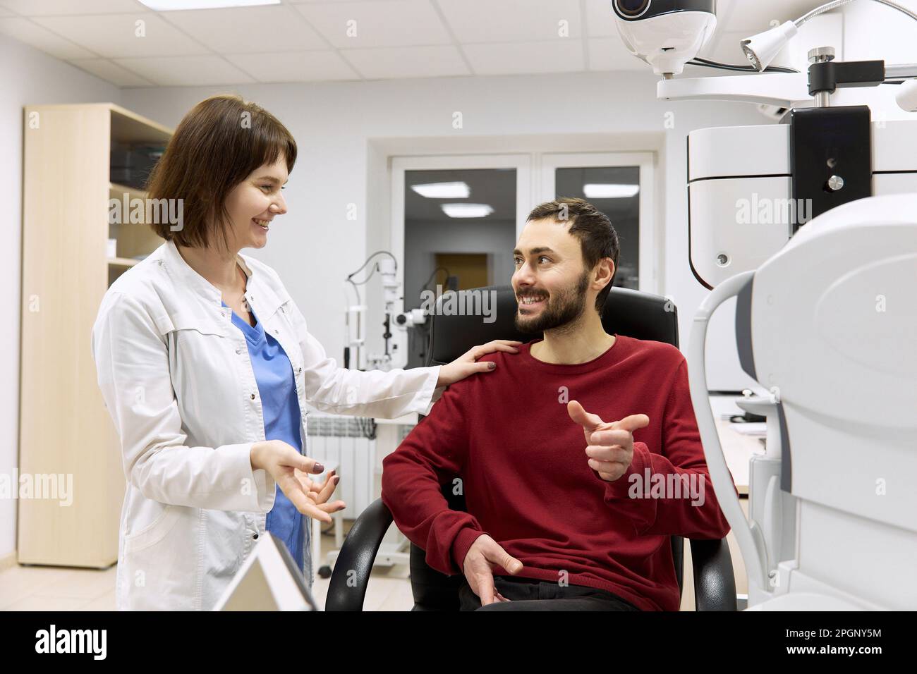 Oftalmologo sorridente che parla con il paziente seduto in clinica Foto Stock