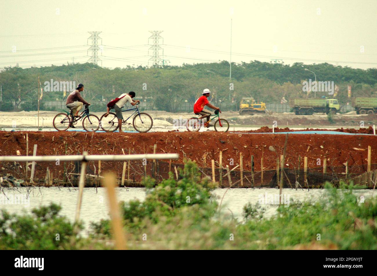 I ciclisti stanno cavalcando su una diga attraverso una zona costiera che è influenzata dallo sviluppo urbano a Giacarta, Indonesia. Foto Stock