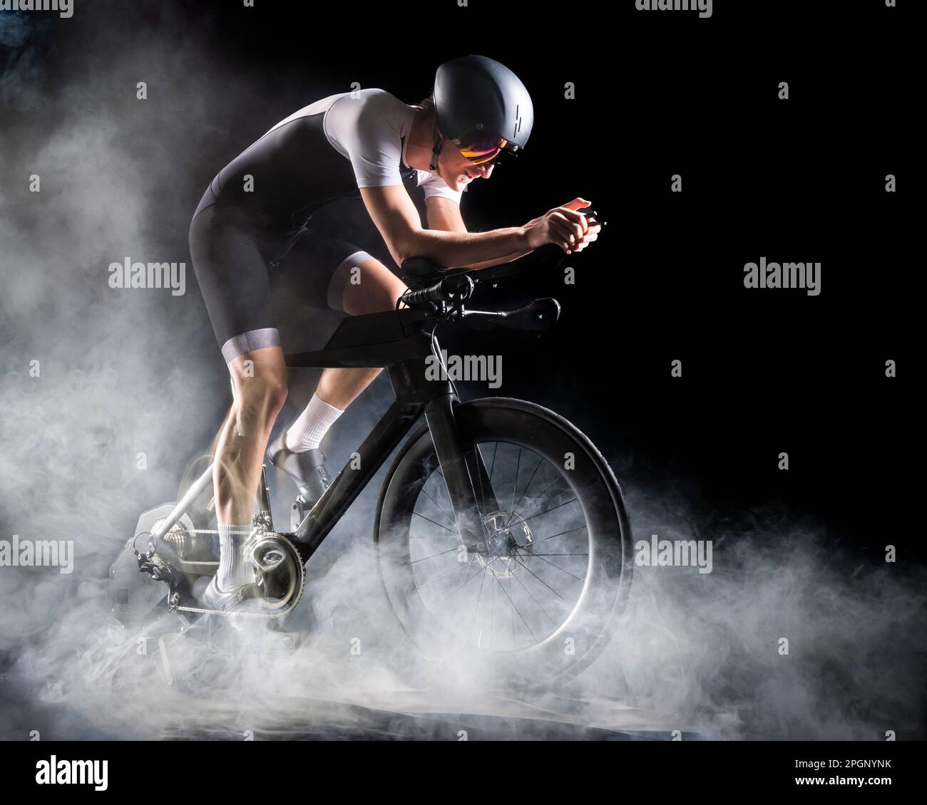 Ciclista indossando abiti sportivi seduti sul turbo trainer su sfondo nero Foto Stock