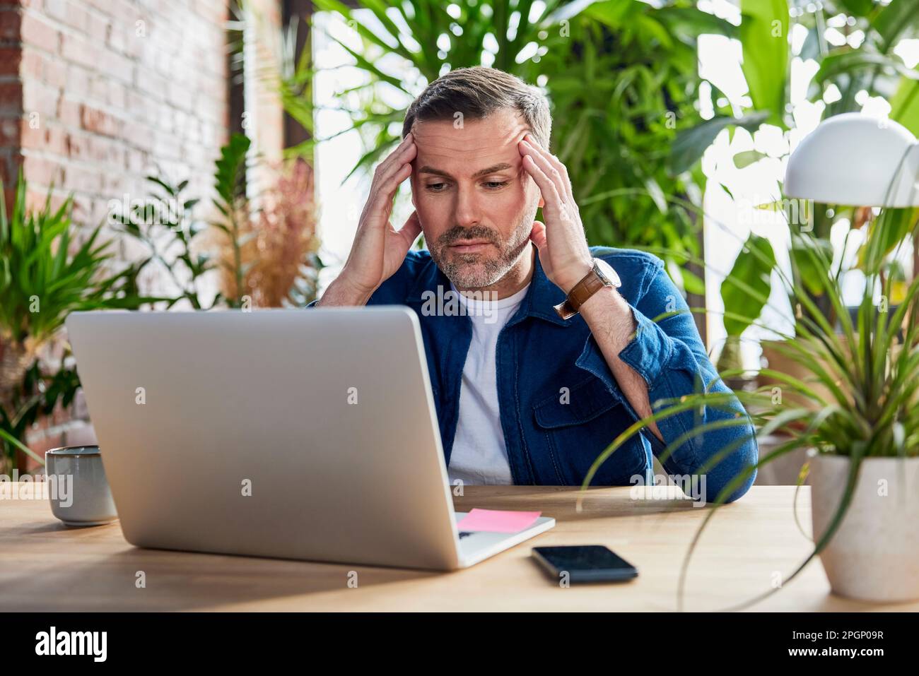 Uomo d'affari preoccupato con un computer portatile alla scrivania in un ufficio loft Foto Stock