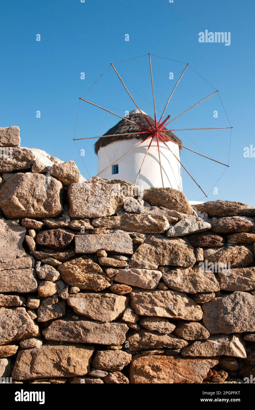 Il mulino a vento di Mykonos è un'icona delle isole Cicladi, apprezzata dai turisti per la sua bellezza e il suo fascino. Incorniciato tra un muro rustico e il cielo blu, Foto Stock