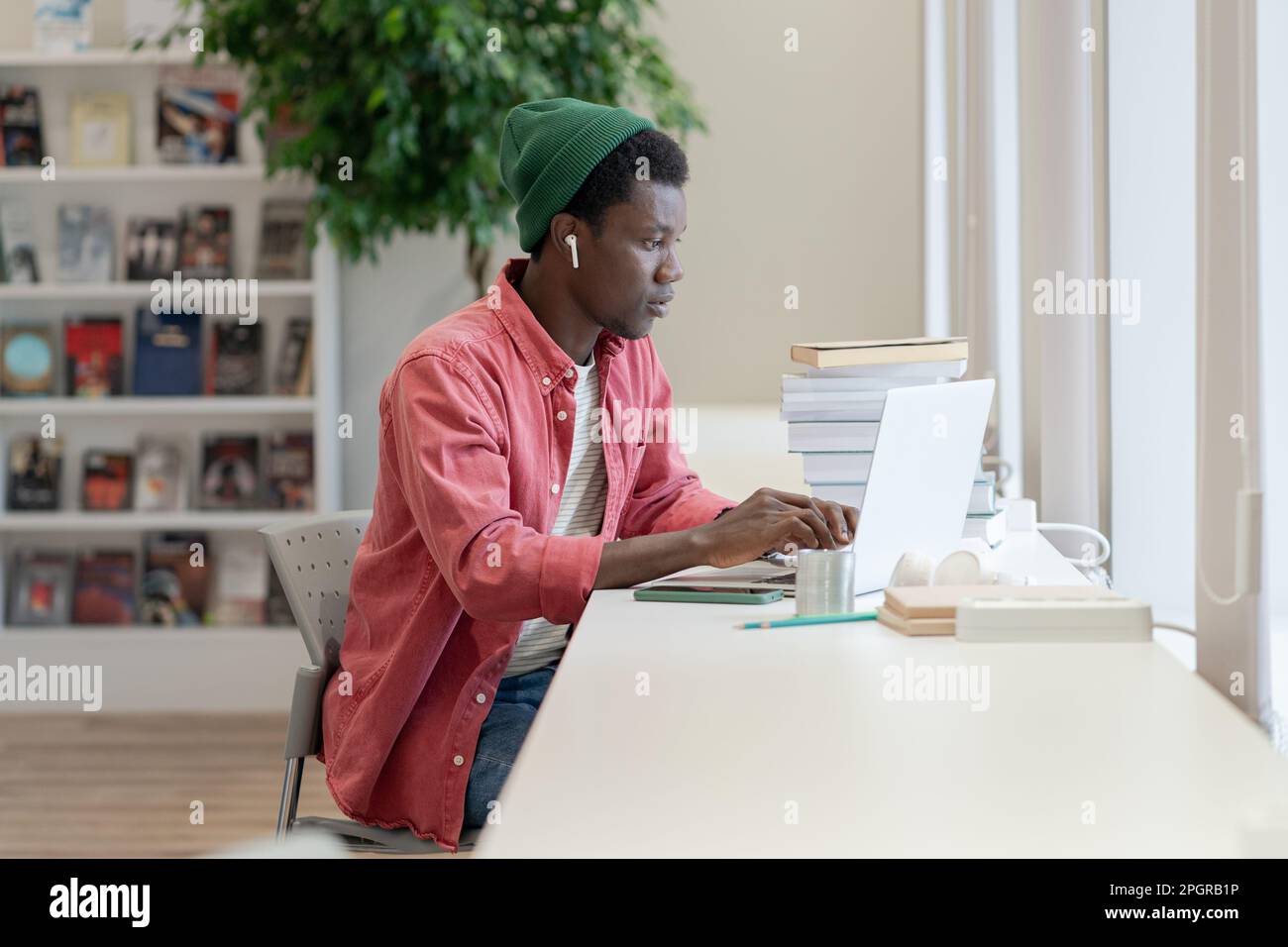 Insegnante di tutor di giovane uomo africano focalizzato che guarda il laptop che si prepara per la classe on-line in biblioteca Foto Stock