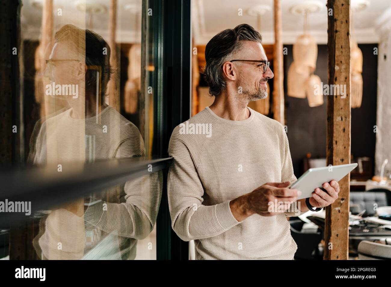 Profilo di bianco allegro uomo di mezza età in occhiali utilizzando tablet computer mentre si lavora in un ufficio moderno Foto Stock