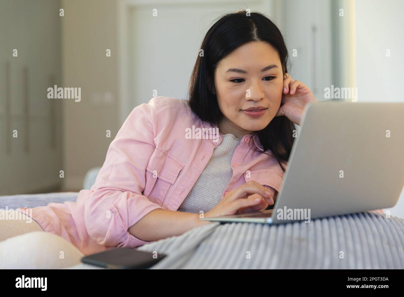 Felice donna asiatica seduta sulla borsa a casa con un computer portatile, sorridente. Stile di vita, relax e comunicazione. Foto Stock