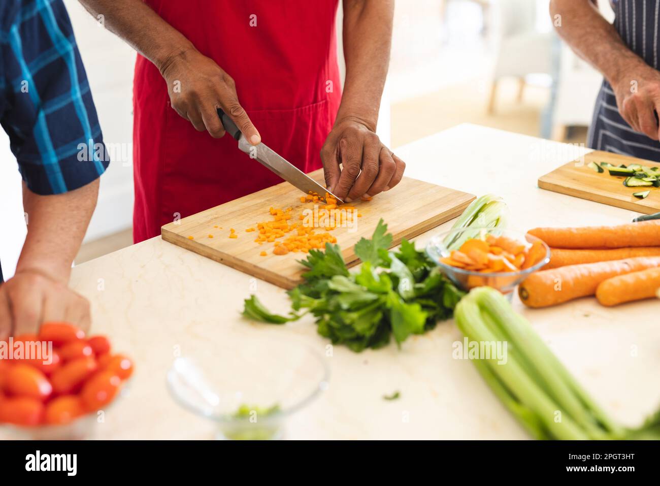 Mani di diversi amici anziani che indossano grembiuli che tagliano verdure durante una lezione di cucina. Pensione, apprendimento, cucina e stile di vita sano. Foto Stock