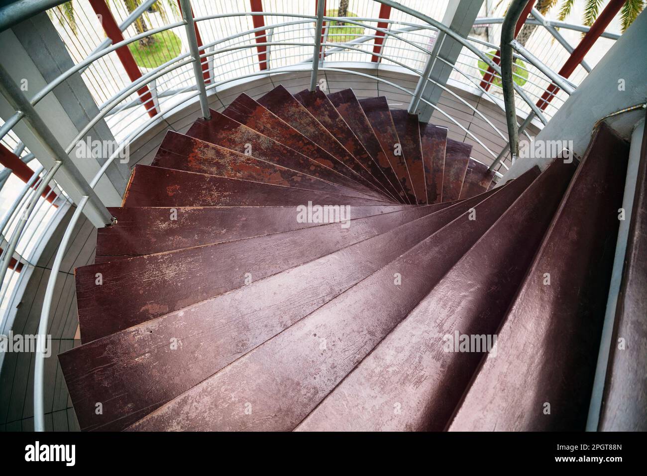 Vista dall'alto di una scala a chiocciola in legno in una torre con finestre. Vecchie scale circolari marroni scabchiate illuminate dalla luce del sole Foto Stock