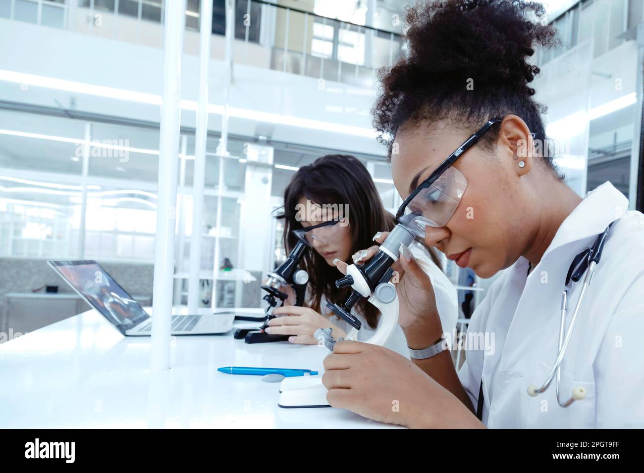 Due studentesse studentesse di dottoressa che osservano il microscopio fa il campione di prova del virus di analisi. giovane specialista in biotecnologia che lavora in laboratorio. scienza medica Foto Stock