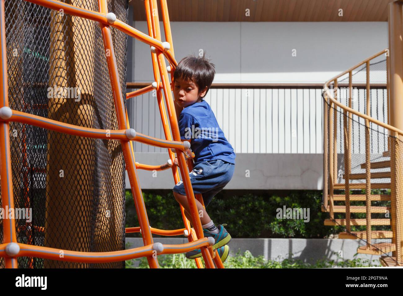 buon ragazzo asiatico giocare sul parco giochi. il ragazzo si arrampica sulla scala nel parco giochi pubblico del parco cittadino durante il fine settimana. Foto Stock