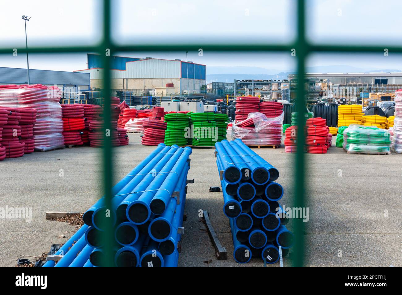 Una vista attraverso una recinzione fino a un magazzino di colorati tubi e materiali in plastica industriale Foto Stock