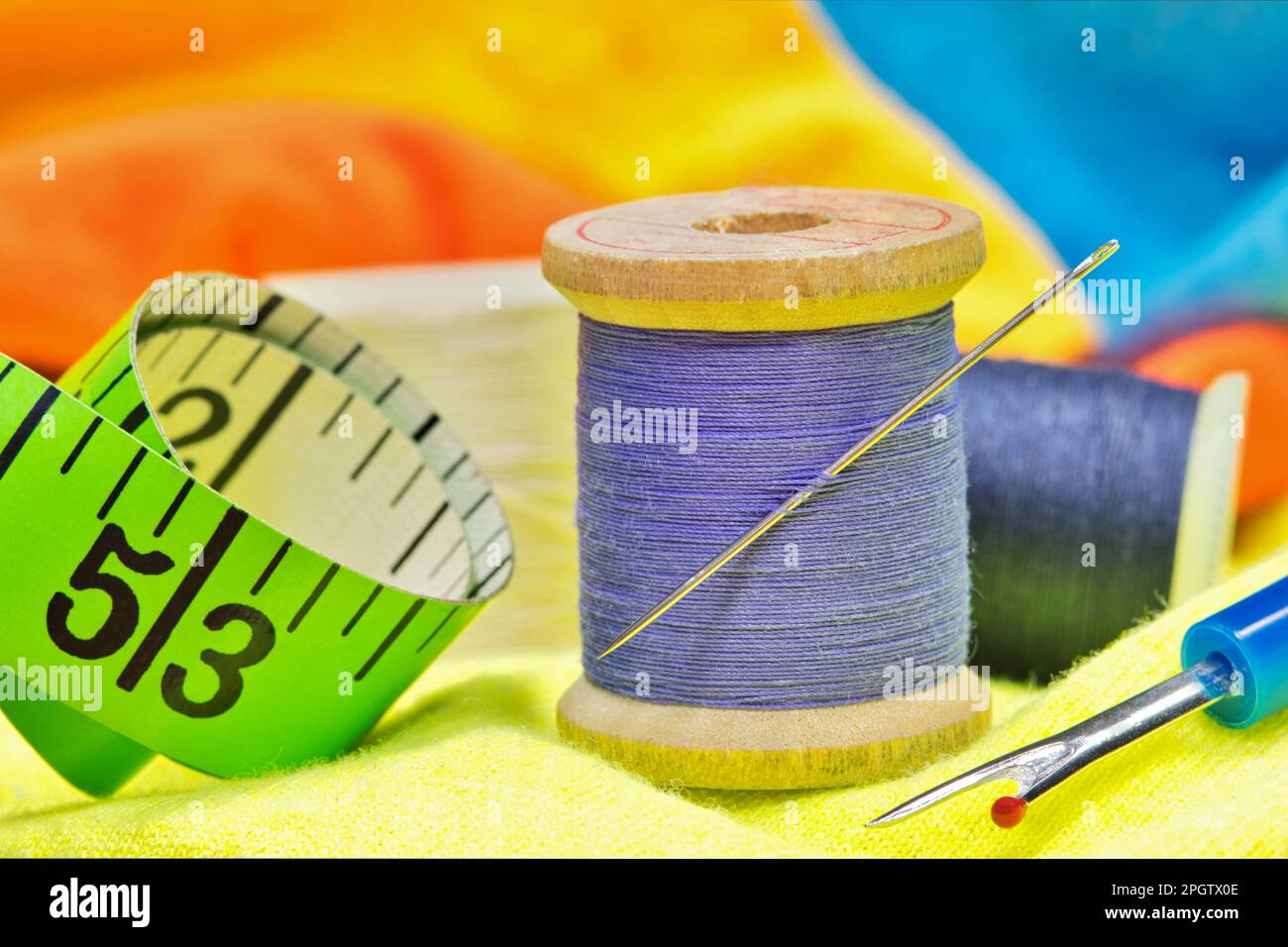 Utensili per cucire su capi colorati con macro dettagli tra cui spole di filo, ago, metro a nastro e raccoglitrice di filo. Foto Stock
