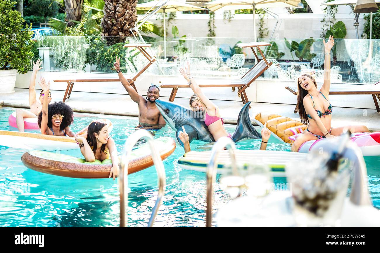 Giovani persone fantasia divertirsi in piscina con letto ad aria lilo e costume da bagno - concetto di stile di vita di lusso con uomini e donne felici godendo summ Foto Stock