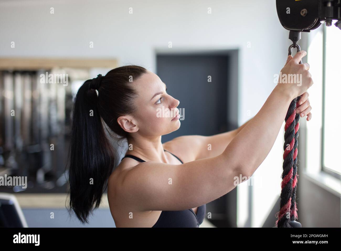 Giovane donna caucasica che appende la corda alla macchina di allenamento in palestra Foto Stock