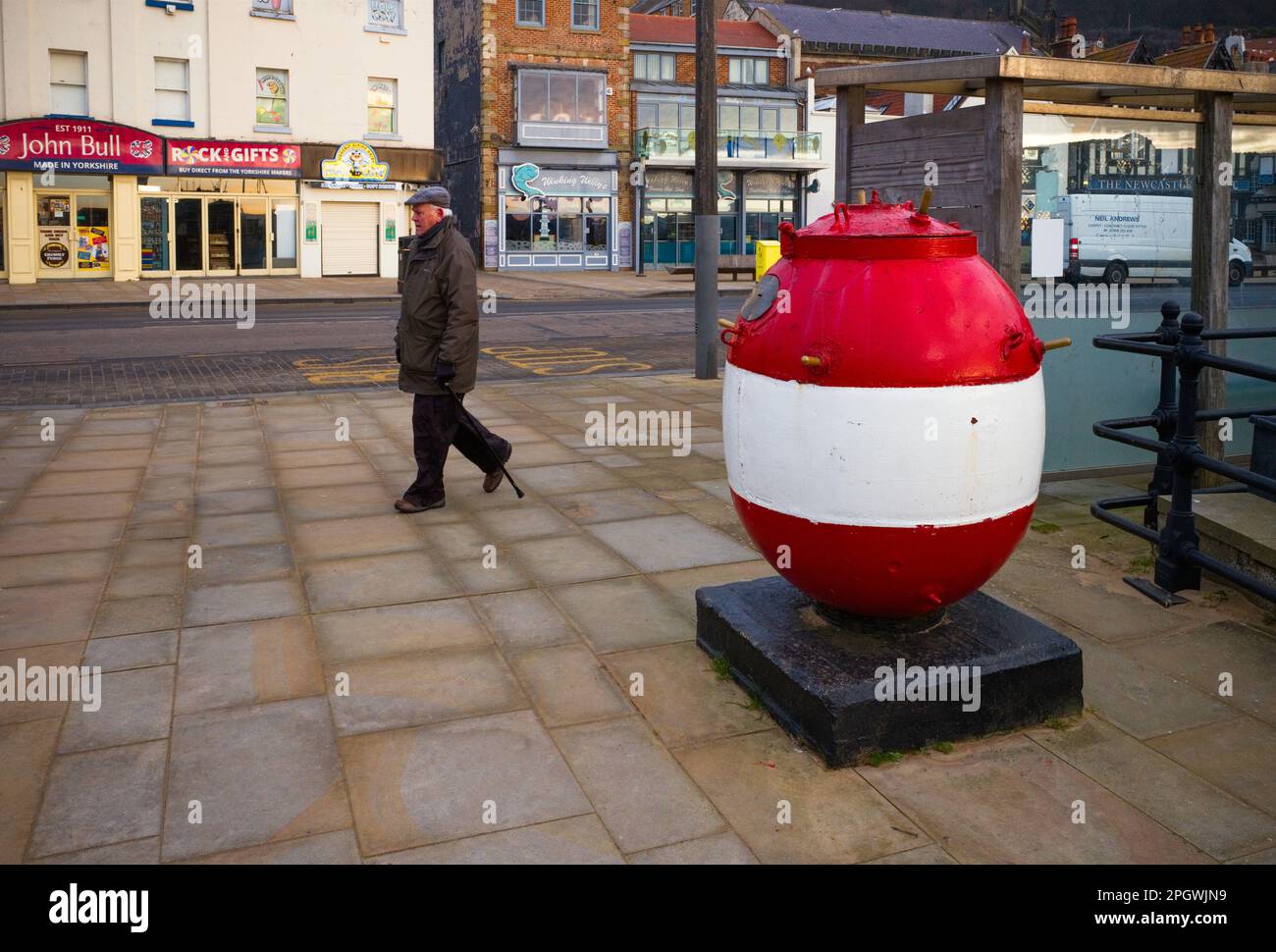 L'uomo più anziano cammina davanti a una scatola di raccolta di carità di miniera di mare sul porto di Scarborough Foto Stock
