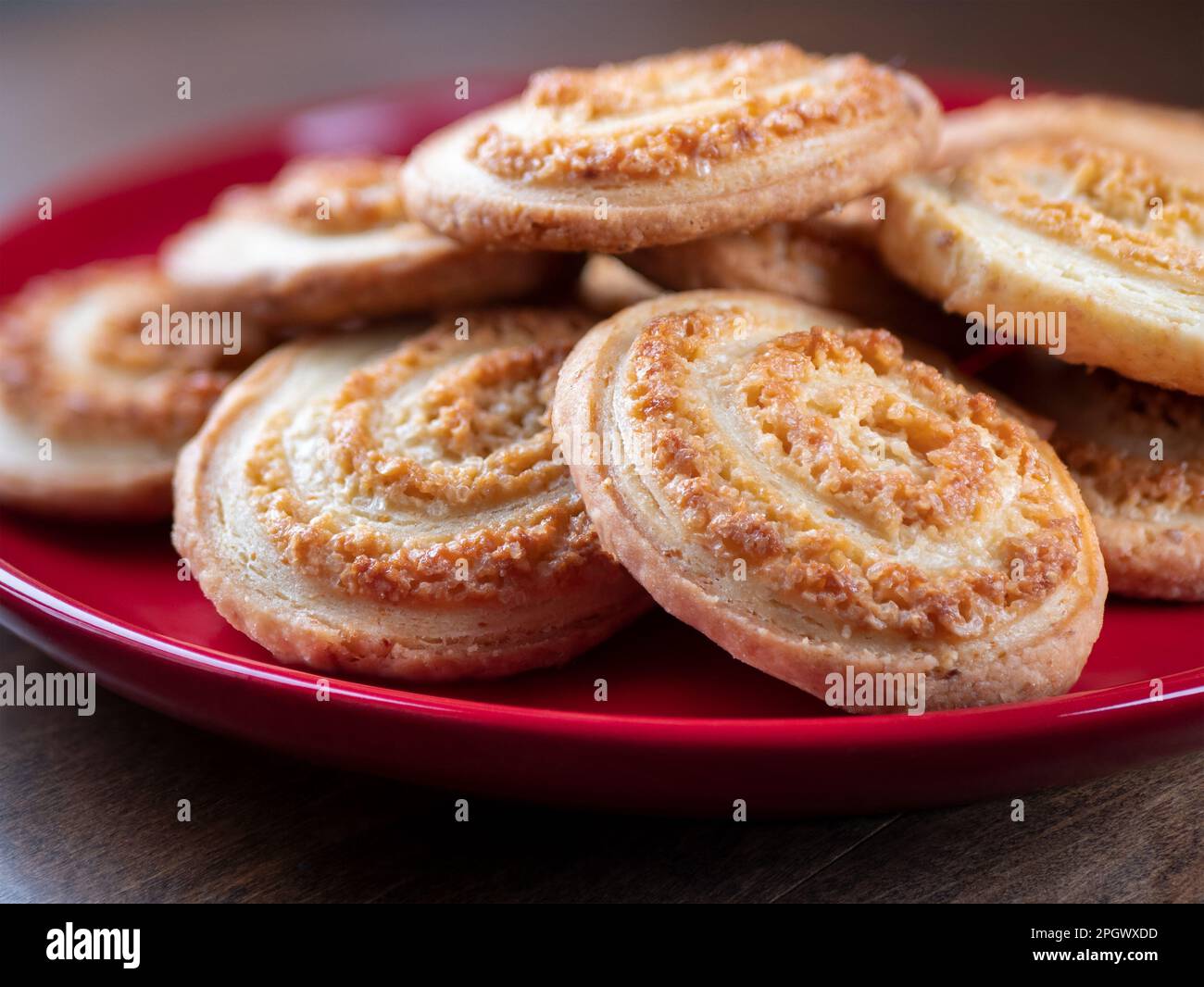 Biscotti a spirale di zucchero su piatto rosso su tavolo di legno, primo piano. Biscotti dolci fatti in casa. Concetto di pasticceria Foto Stock