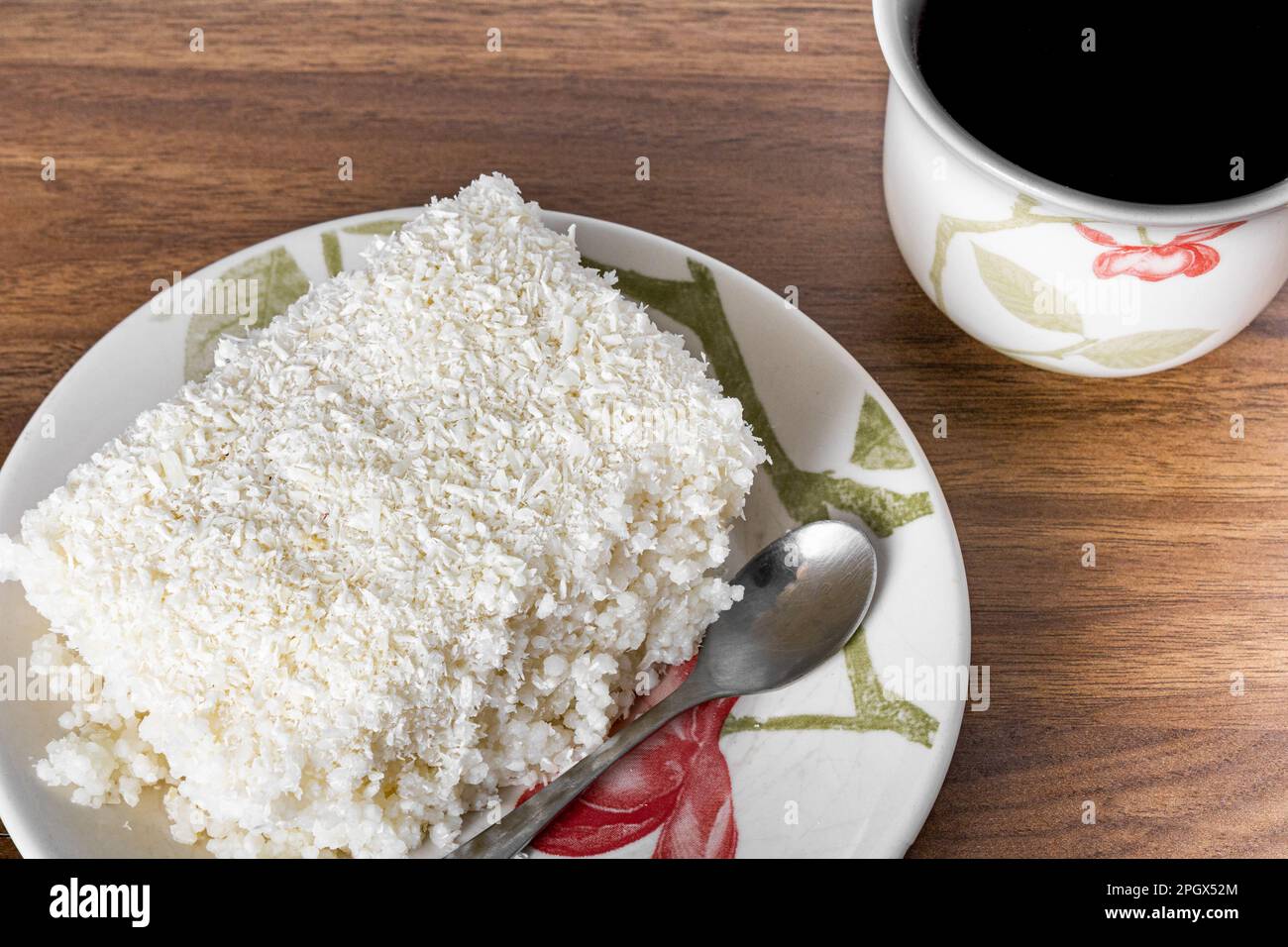 Couscous in piattino di porcellana su tavolo di legno, piatto tipico brasiliano, fatto con tapioca, latte, zucchero e latte di cocco. Con tazza di caffè. Foto Stock