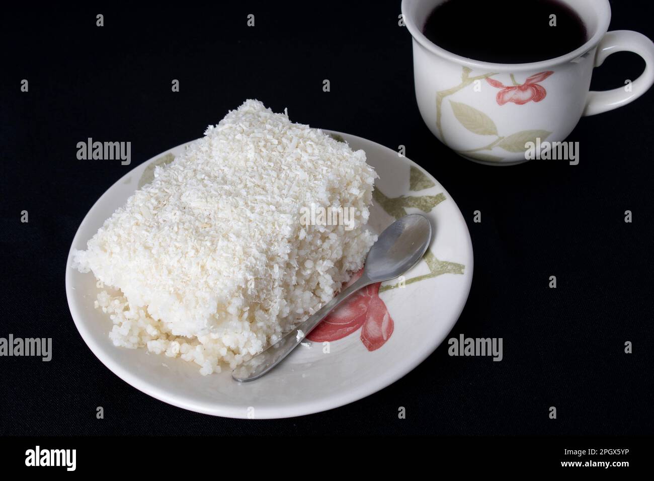 Couscous in piattino di porcellana su fondo nero, piatto tipico brasiliano, realizzato con tapioca, latte, zucchero e latte di cocco. Con una tazza di caffè Foto Stock