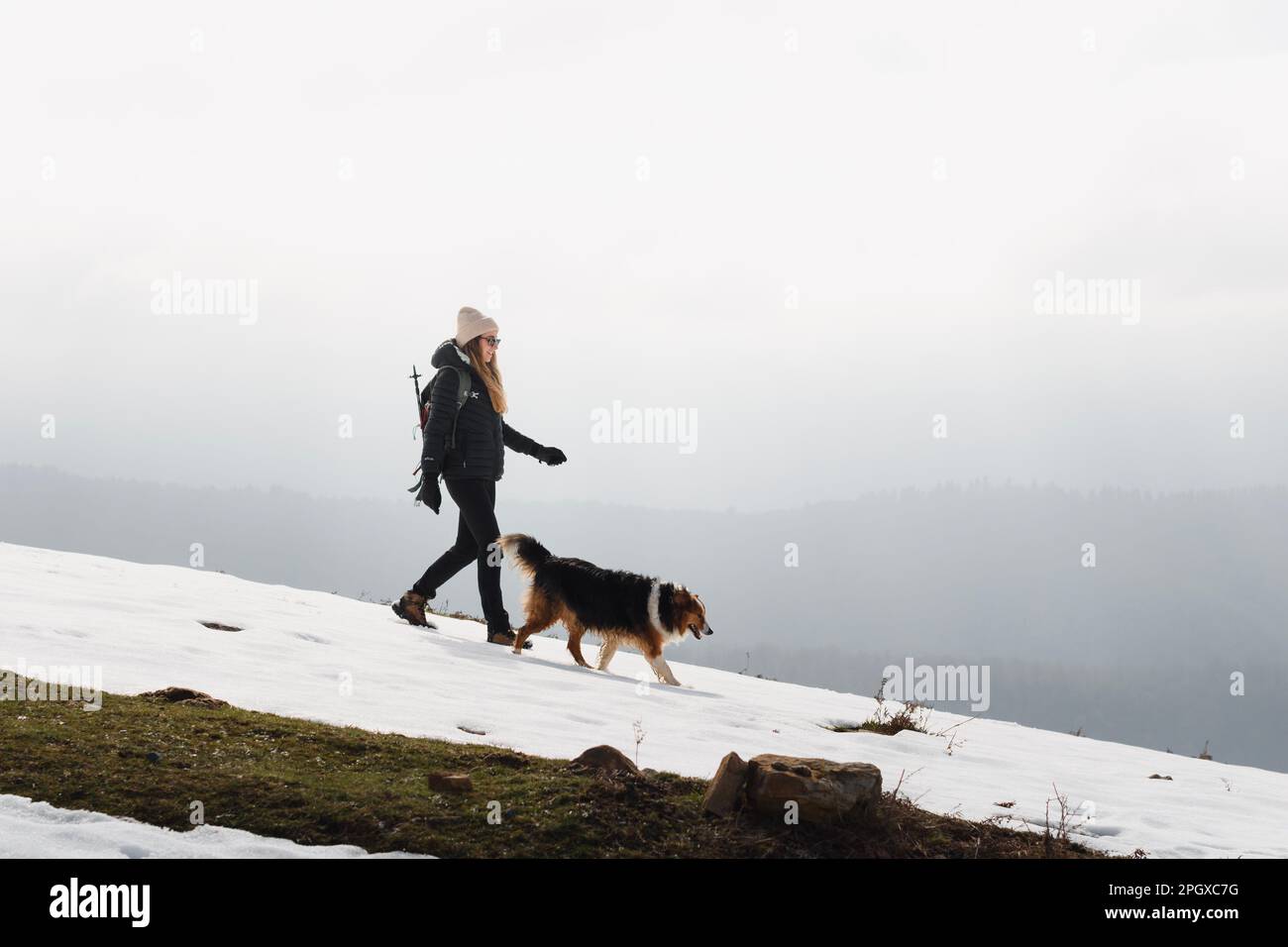 Ragazza con abiti invernali che cammina con il suo cane sulle montagne coperte di neve Foto Stock
